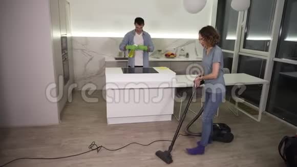 清洁日年轻夫妇打扫他们的公寓戴手套的男人擦拭厨房炉子女孩用清洁地板视频的预览图