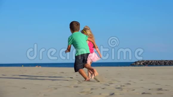穿着粉红色裙子的小男孩和女孩正在海滩上玩追赶游戏视频的预览图