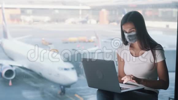 戴防护医疗面罩的妇女使用笔记本电脑在机场工作视频的预览图