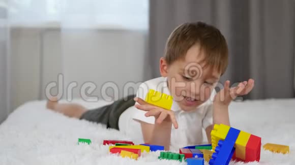 快乐快乐的男孩躺在床上玩彩色积木一个孩子从meccano那里建立起来视频的预览图