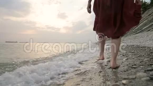 近景后景的双腿白种人女孩走在海边的石头海岸的水中走向夕阳视频的预览图