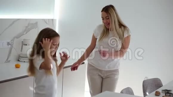 幸福的家庭在现代白色的厨房妈妈和女儿穿着白色便服放松充分跳舞和唱歌妈妈是视频的预览图