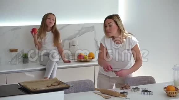 嘲笑妈妈和女儿一起玩女孩坐在厨房的柜台上一边吃苹果一边妈妈在安排视频的预览图