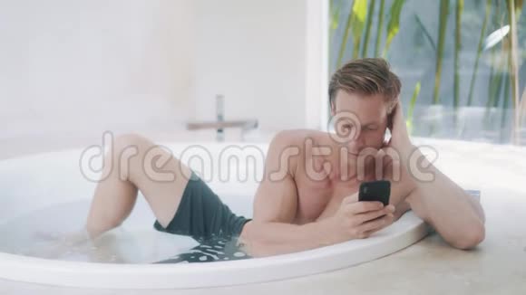 年轻人在现代浴缸里用智能手机阅读信息视频的预览图
