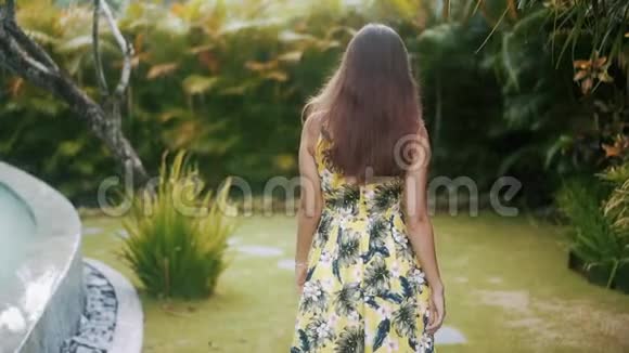 女人穿过热带花园走向镜头用手抚摸头发微笑视频的预览图
