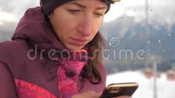有魅力的年轻女子在一个滑雪胜地站在雪地上用手机视频的预览图