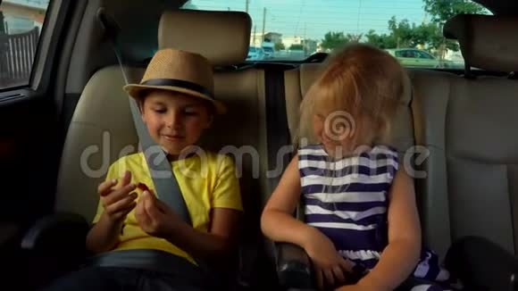 小男孩和一个戴着帽子的金发女孩正在车后座玩耍视频的预览图