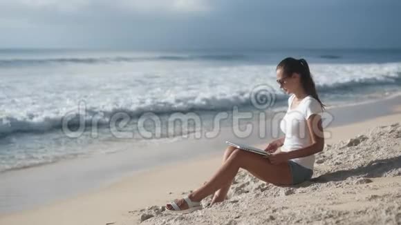 戴太阳镜的女人在沙滩上用笔记本电脑工作打开它开始打字视频的预览图