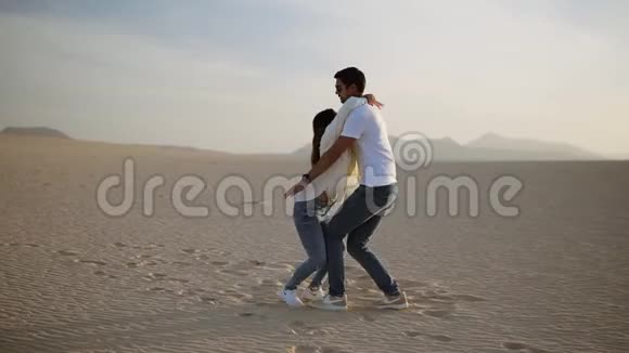 在空旷的沙漠中年轻夫妇的完美场景男人抱着她的女人把她转过来玩得开心视频的预览图