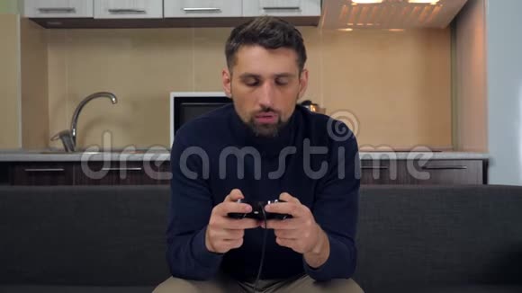 穿着深蓝色套头衫和灰色裤子的沮丧的年轻人放下一个游戏垫从沙发上站起来离开视频的预览图