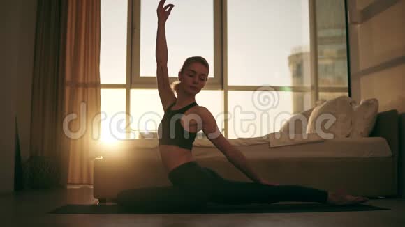 金发白种人的女人在家里练习瑜伽坐在地板上的黄色垫子上变换姿势鸽子姿势视频的预览图