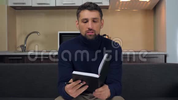 男人坐在沙发上用黑色钢笔在笔记本上写任务目标梦想和想法视频的预览图