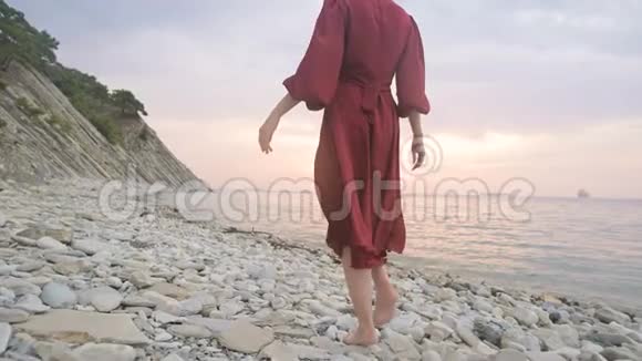 在日落时分一个穿着红色裙子在风中飘舞的赤脚女孩的腿后特写慢动作视频的预览图