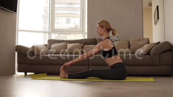 金发穿着黑色紧身裤和运动胸罩的白种人坐在训练席上做瑜伽或伸展身体视频的预览图