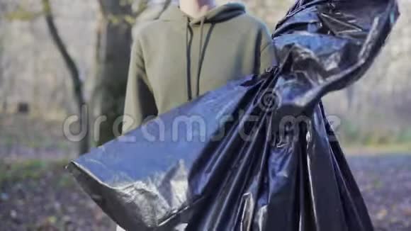 一个女志愿者展示像和一个黑色垃圾袋清除森林的塑料环境问题视频的预览图