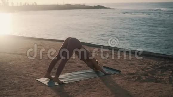 有技巧的女孩在海滩上用向下的狗瑜伽姿势抬起腿视频的预览图