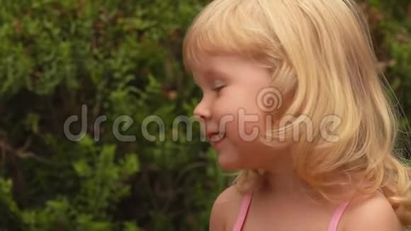 一个金发女孩在阳光明媚的公园户外微笑的肖像视频的预览图