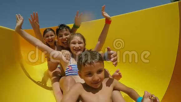 快乐的男孩和女孩正在水上公园里沿着橙色的滑梯骑着视频的预览图