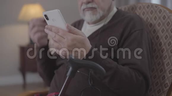 无法辨认的老人在智能手机上打开播放列表用耳机听音乐积极的成熟退休人员视频的预览图