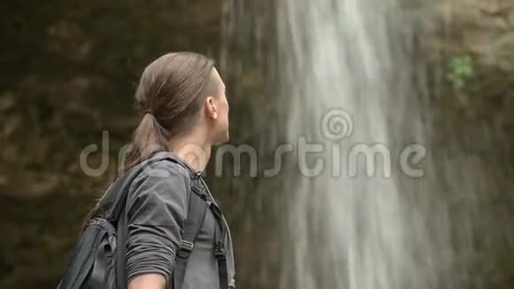 年轻的旅行者站在瀑布的背景上环顾四周特写视频的预览图