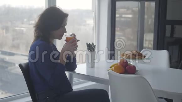 自信的高加索女人闻到橙汁和吃水果的侧面景色富有的女商人在吃早餐视频的预览图
