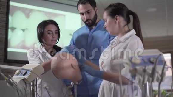 英俊的中东牙医向助手展示如何在口腔中使用设备高加索女性在练习视频的预览图