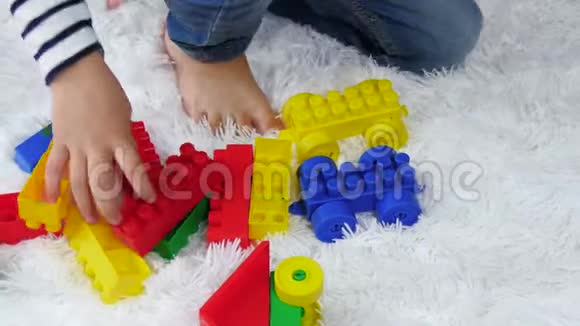 一个小男孩坐在地板上的白色地毯上玩着五颜六色的积木大会视频的预览图