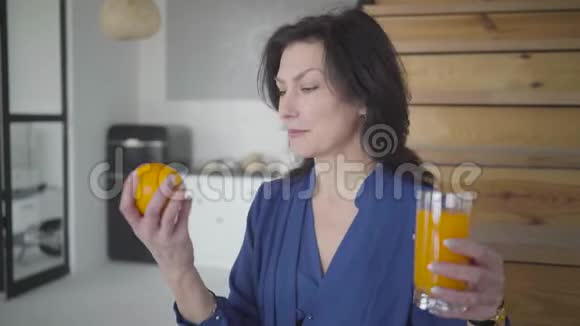 积极优雅的白种人女人手里拿着果汁和橘子对着镜头微笑优雅成人的肖像视频的预览图