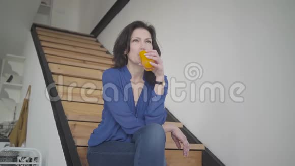 在家的楼梯上喝橙汁的优雅白种人女人的底部景色成功的成年商人视频的预览图