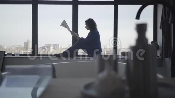 严肃的高加索女商人坐在窗台上看报纸侧景照片成年黑发女子视频的预览图