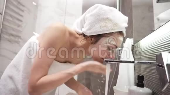 一个女人站在洗手池附近头上戴着白色毛巾身体上用白色化妆面具洗了一个白色的面具视频的预览图