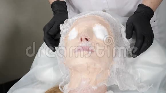 化妆程序美容师从女性病人脸上取出硬化面罩在面具下移动的脸水疗和美容视频的预览图