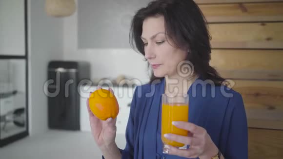 一位成年白种人深色头发的女士她用手检查橘子和果汁并用相机拍摄水果和玻璃视频的预览图