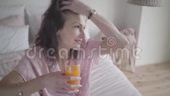 美丽的黑发白种人女人的脸调整头发和微笑手里拿着橙汁的快乐女士视频的预览图