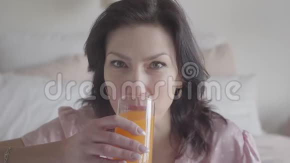 迷人的白种人女人喝着橙汁对着镜头微笑积极的黑发女人视频的预览图