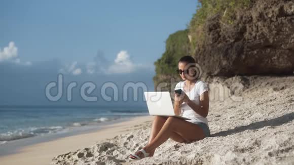 戴着太阳镜的女自由职业者在海滩上工作带着笔记本电脑打电话聊天视频的预览图