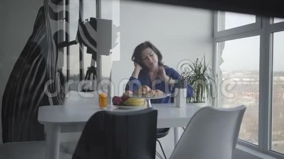 摄影棚拍摄的快乐的成年白种人女人早上在室内吃早餐微笑着的黑发女人视频的预览图