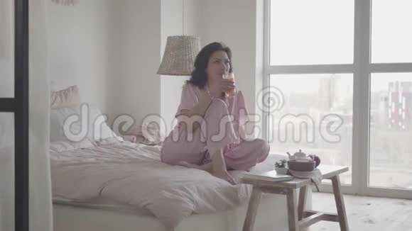 年轻的白种人黑发女人在早晨享受新鲜橙汁的肖像美丽的女士喝有机饮料视频的预览图