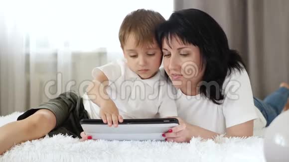 母子俩在平板电脑上看电影躺在沙发上幸福家庭养育子女工作的概念视频的预览图