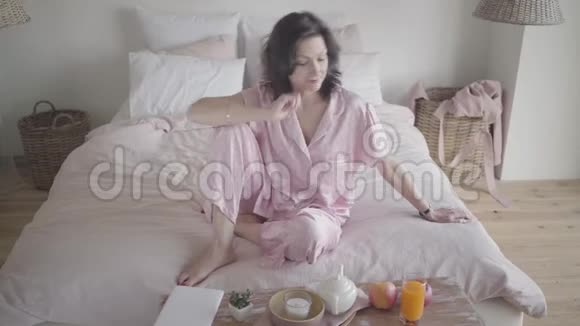 快乐迷人的白种人女人穿着粉红色的睡衣拿着橙汁喝玻璃好漂亮的女人视频的预览图