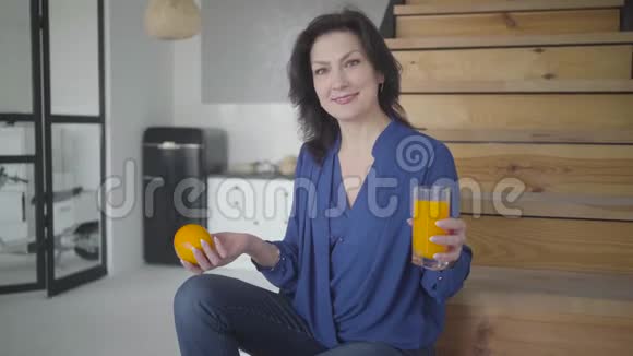 积极成功的白种人女人拿着橘子和玻璃杯拿着果汁对着镜头微笑的肖像快乐视频的预览图