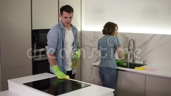 年轻的已婚夫妇穿着休闲服装搬到新家后两人都戴着绿色手套打扫厨房视频的预览图