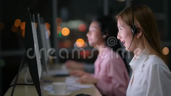 漂亮的亚洲接线员女孩工作然后看着相机在晚上和团队一起工作时微笑视频的预览图