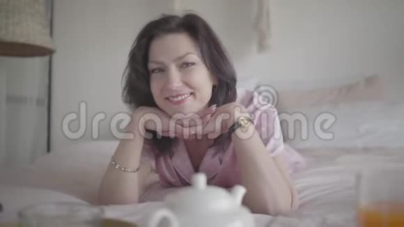 积极的白种人黑发女人在卧室早上摆姿势的肖像可爱的小姐躺在床上视频的预览图