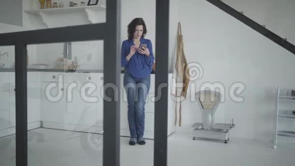 宽镜头优雅的白种人妇女滑动智能手机屏幕和饮用有机橙汁自信的肖像视频的预览图