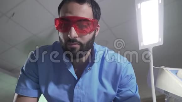 专业的中东牙医使用相机上的仪器戴防护眼镜和手套的人的肖像视频的预览图
