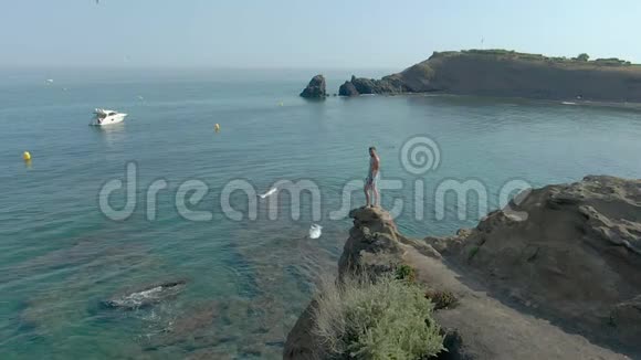 年轻人站在清澈的海面上的悬崖上背景是船视频的预览图