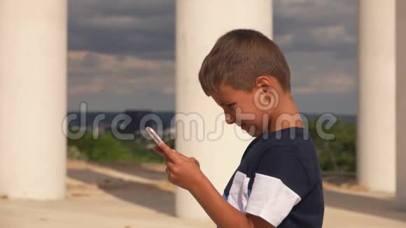 严肃的男孩正在观看白色柱子背景下的电话视频的预览图