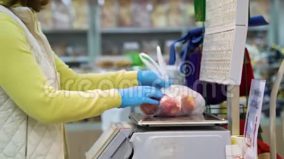 女顾客戴着医用手套在杂货店里用秤称苹果视频的预览图