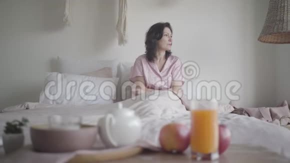 深色白种人女人穿着睡衣坐在床上的肖像积极的女士在家享受周末视频的预览图